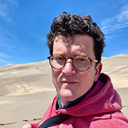 Photograph of Jay Holley sitting in front of the Colorado sand dunes